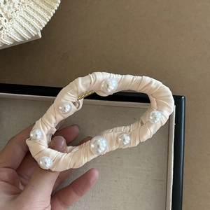 Gros plan sur une grande pince à cheveux en satin crème ornée de perles et tissu plissé
