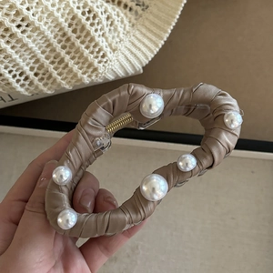 Détail d'une élégante pince à cheveux en satin champagne avec perles et tissu plissé
