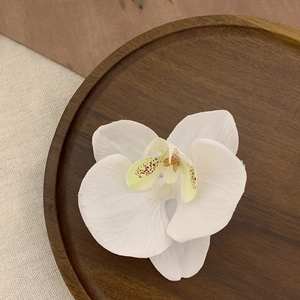 Detailed close-up of a white phalaenopsis orchid hair clip on a rustic wooden tray