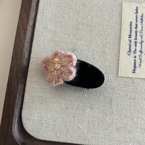 Détail d'une barrette fleur tricotée rose avec perles jaunes sur velours noir