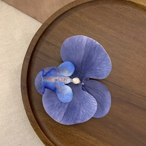 Close-up of a realistic purple and blue orchid hair clip on a wooden tray
