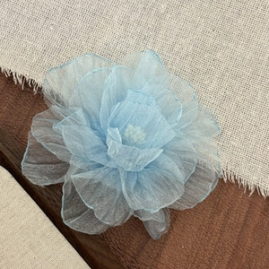 Close-up of light blue fabric flower hair clip with translucent layers on wood