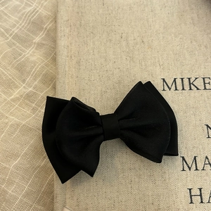 Elegant double-layered black satin bow hair clip on a beige textured background