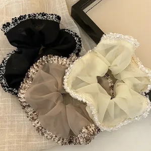 Drei Organza-Haargummis in Schwarz und Beige mit gewebter Bordüre auf strukturiertem Stoff