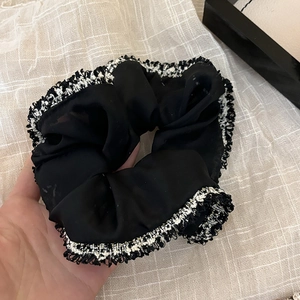 Detail eines schwarzen Organza-Haargummis mit eleganter Tweed-Borte und Fransenrand