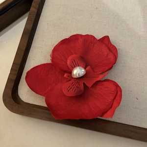 Détail d'une pince à cheveux orchidée rouge en soie avec perle sur plateau