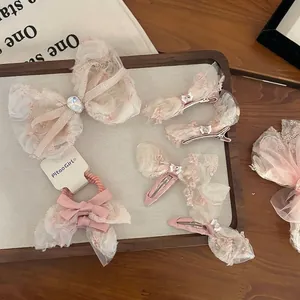 Pink silk bow hair clips and lace scrunchies set with rhinestone accents on a wooden tray