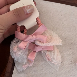 Detailed close-up of pink lace and satin bow hair ties on a white card display