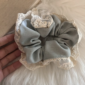 Détail d'un chouchou bleu clair avec bordure en dentelle crème sur fond moelleux