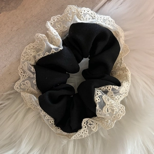 Gros plan d'un chouchou en tissu noir avec bordure en dentelle beige sur fond en peluche