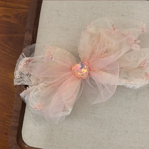 Close-up of pink lace bow hair clip with layered mesh and heart-shaped gemstone