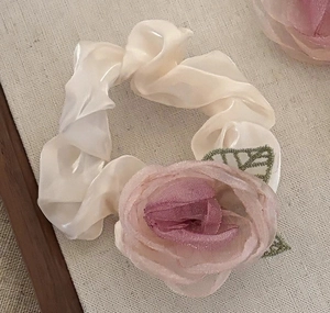 Detaillierte Makroansicht eines cremefarbenen Satin-Haargummis mit einer rosa Organza-Rose