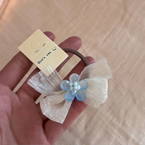 Détail de pince à cheveux avec nœud en tulle blanc et fleur en résine bleu clair sur carte