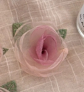 Detail einer handgefertigten Mesh-Kamelienblüte mit zarten grünen Spitzenblättern