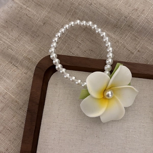 Detailed shot of white plumeria flower hair clip with pearls on a wooden tray