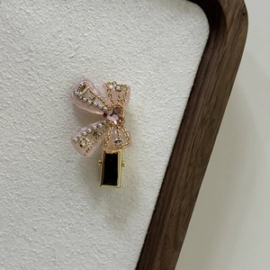 Detail of pink bow hair clip with faux pearls and heart-shaped gemstone on gold base