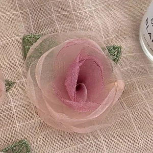 Rosafarbener Stoff-Kamelien Haarschmuck mit grünen Blättern auf Leinenhintergrund