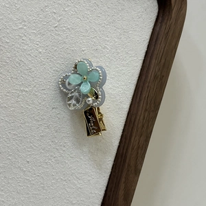 Detail of blue flower hair clip with pearls and Hand Made engraving on gold metal base