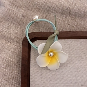 Detailed view of white frangipani hair tie with blue elastic band and pearl bead accents