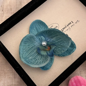 Vue détaillée de la barrette orchidée bleu foncé avec perle centrale et texture tissu