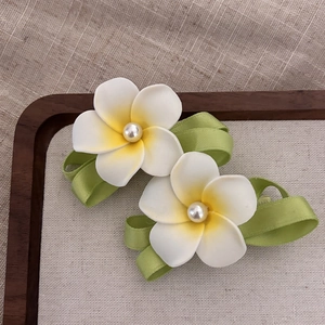 Handmade plumeria hair clips with white beads and green ribbons on wood board