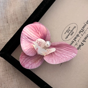 Vue macro d'une pince à cheveux orchidée avec pétales rose violet et une perle blanche