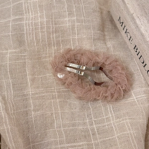 Détail d'une pince à cheveux en tulle plissé crème avec base en métal argenté sur tissu