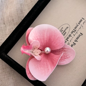 Détail d'une pince à cheveux orchidée rose avec perle sur un support vintage français