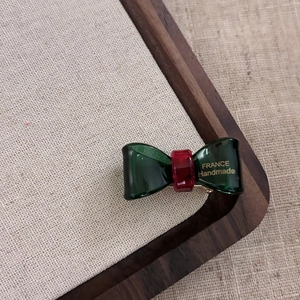 Durchscheinende grüne Azetat-Haarklammer mit Goldlogo auf einem Holz-Schmucktablett