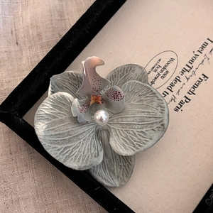 Détail macro d'une pince orchidée avec pétales en tissu gris tacheté et perle blanche