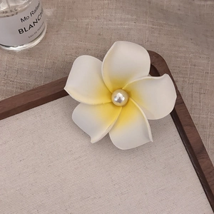 Macro shot of a white frangipani hair clip with yellow gradient and center pearl detail