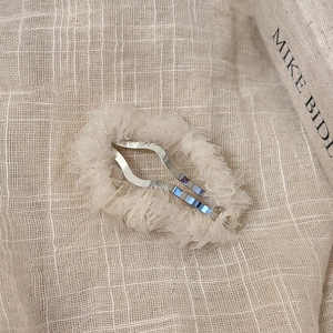 Détail d'une pince à cheveux plissée en gaze beige champagne avec base en métal argenté