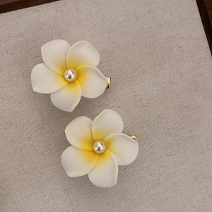 Detail of two white frangipani hair clips with yellow centers and pearls on linen