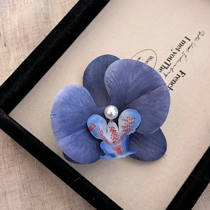 Détail d'une pince à cheveux orchidée bleue avec pétales en tissu et perle blanche centrale
