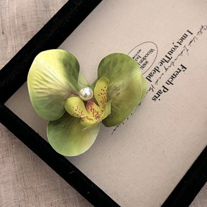Gros plan d'une pince à cheveux orchidée aux pétales verts et perle centrale