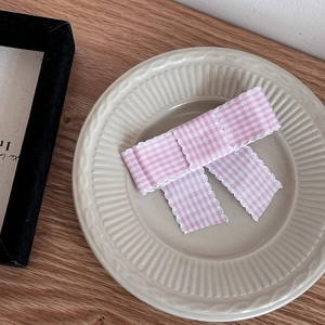 Close-up of a pink and white checkered bow hair clip on a vintage ceramic tray