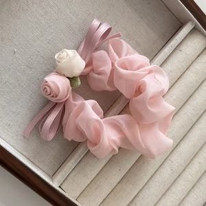 Détail d'un chouchou en tissu avec roses rose et beige et nœud en satin dans un coffret