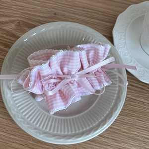 Detail of pink plaid scrunchie with lace pleats and satin bow on a ceramic plate