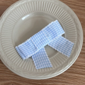 Detailed view of light blue gingham bow hair clip with white wavy lace trim on a plate