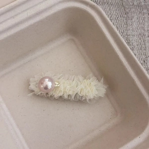 Detail einer cremefarbenen Spitzenhaarspange mit rosa Kunstperle auf Tablett
