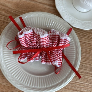 Preppy style red and white plaid scrunchie with a large bow and long ribbons on a ceramic plate