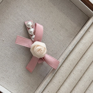 Détail d'une barrette à cheveux en satin rose avec perles nacrées et rose en tissu blanc