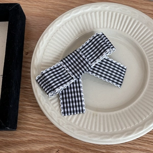 Close-up of black and white checkered bow hair clip with textured wavy edges on a ceramic plate