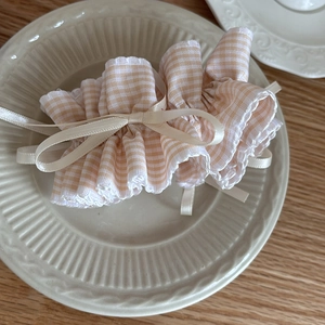 Gingham hair scrunchie with beige silk bow and ruffled edges on a ceramic plate