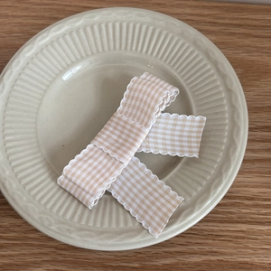 Detail of pink and white checkered bow hair clip with scalloped edges on a ceramic plate