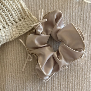 Détail du chouchou en satin champagne avec petits nœuds sur fond de tricot doux