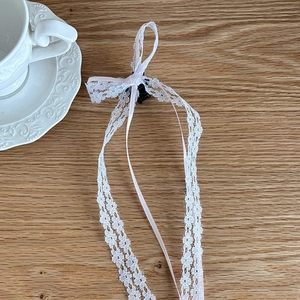 Detailed macro of a light pink lace bow hair clip with long ribbons on wooden surface