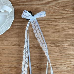 Detailed view of white lace bow hair clip with long ribbons on a rustic wooden table
