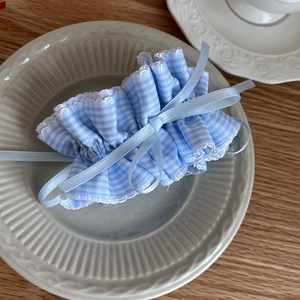 Detail of blue plaid ruffled scrunchie with long ribbon bow on white ceramic plate