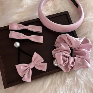 Ensemble de cinq accessoires de cheveux en satin rose avec perles dans un plateau bois